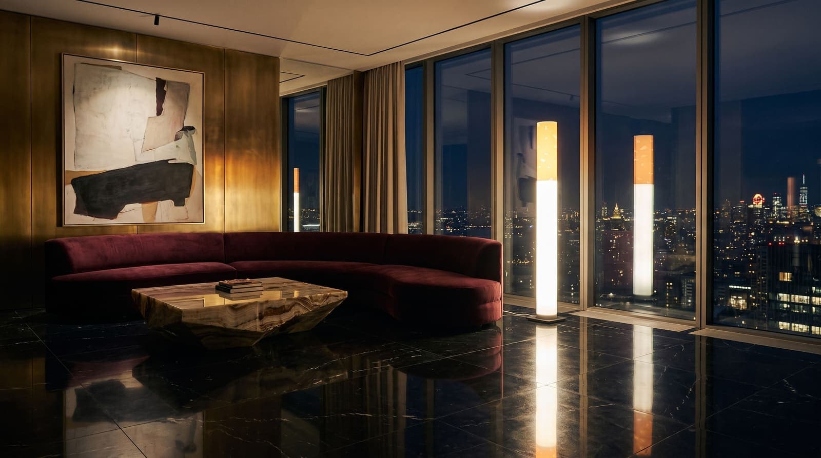 The floor lamp glowing in a penthouse salon of black marble and brass with a burgundy curved sofa and city lights behind