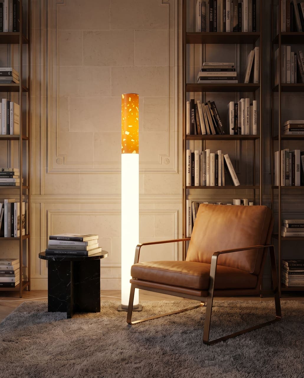 The lit floor lamp beside a caramel leather lounge chair, a black marble side table and tall bronze bookshelves