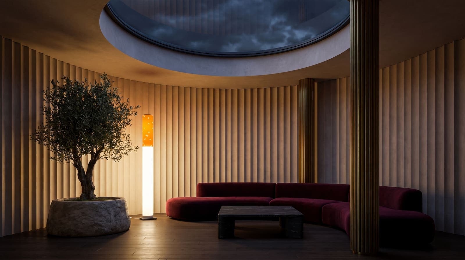 The floor lamp glowing beside an olive tree in a round salon of fluted plaster under a circular skylight, a burgundy velvet sofa curving with the wall